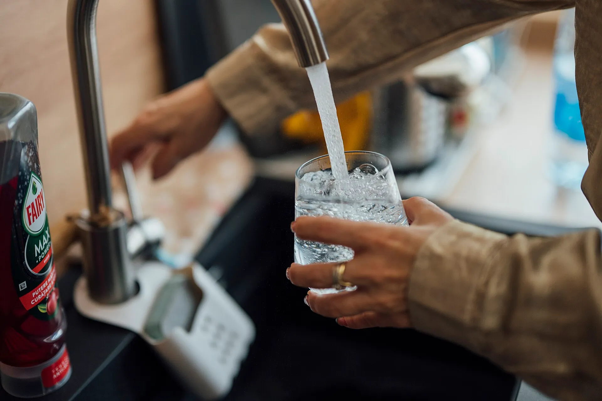 Person filling a glass with water at a kitchen sink